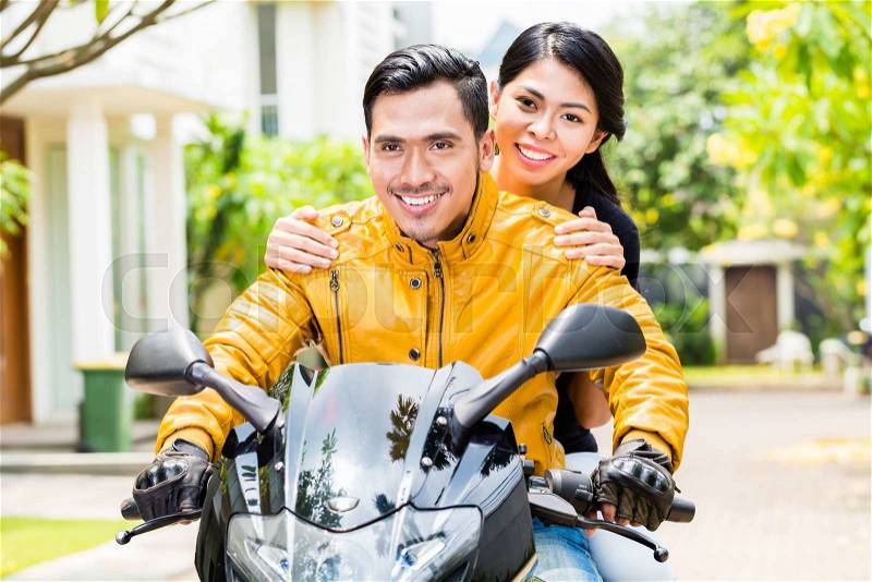 Asian couple riding motorcycle, wife is sitting behind her husband, stock photo