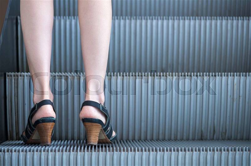 Business woman in high heels standing on escalators stairway, stock photo