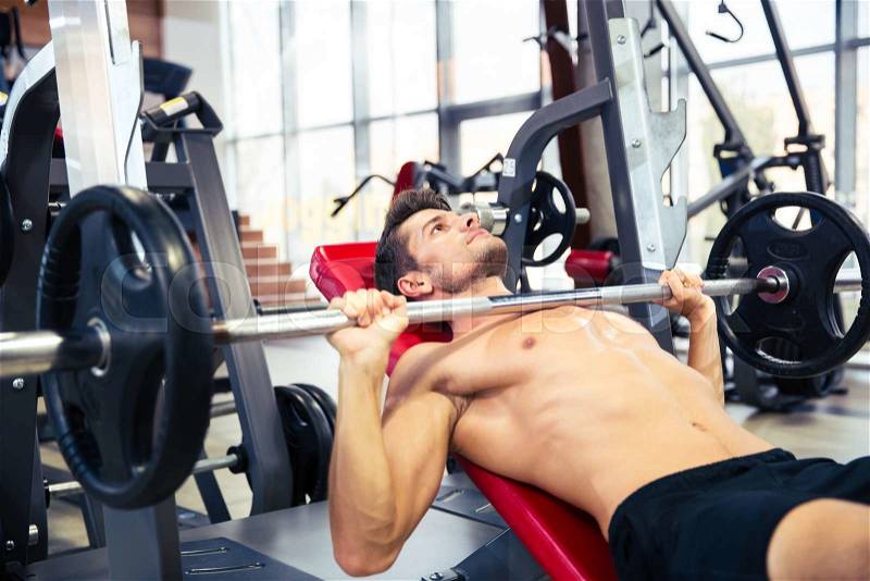 Portrait of a fitness man workout with barbell on the bench at gym, stock photo