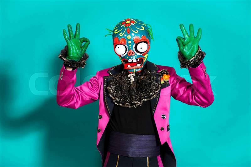 Circus actor in zombie suit posing on studio background.Scary man wearing green spooky skeleton mask,pink jacket,black pants,gloves. Halloween party time, stock photo