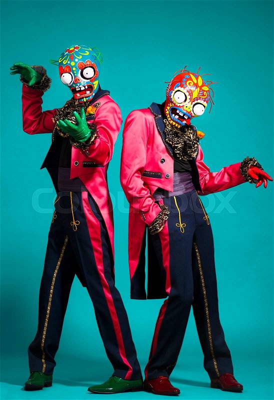 Two circus actors in zombie suit posing on studio background.Scary men wearing green spooky skeleton mask,pink jacket,black pants,gloves. Halloween party time, stock photo