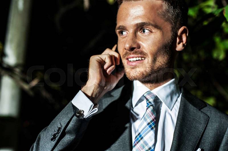 Portrait of handsome bearded man in classical elegant suit poses on street at night.Businessman speaks phone.Fashion look, stock photo