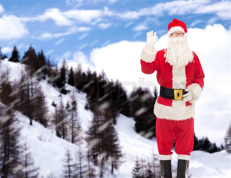Christmas, holidays, gesture and people concept - man in costume of santa claus waving hand over snowy mountains background, stock photo