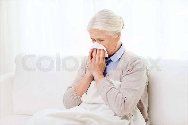 Health care, flu, hygiene, age and people concept - sick senior woman blowing nose to paper napkin at home, stock photo