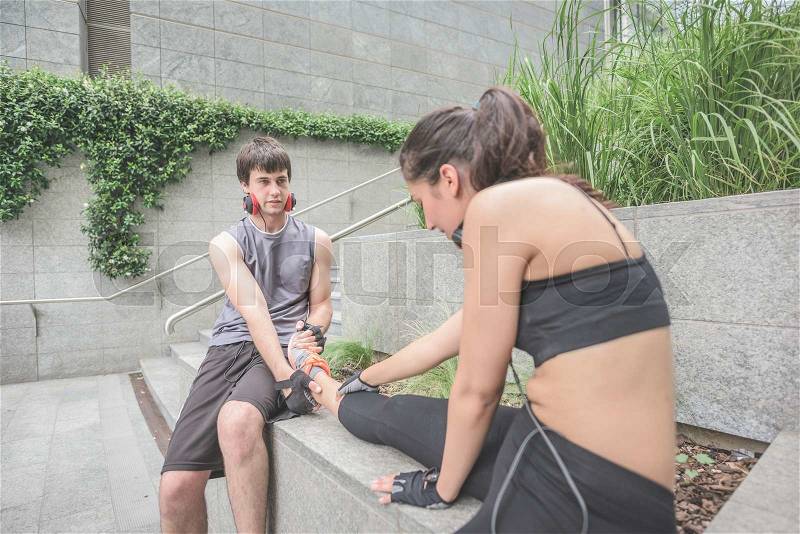 Couple of young hansome caucasian sportive man and woman helping each other stretching - he helps her to stretch her leg, both looking downward, focus on the man - sportive, fitness, healthy concept, stock photo