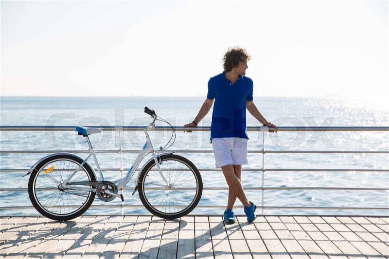 Full length portrait of a handsome man with bicycle resting outdoors near the sea, stock photo