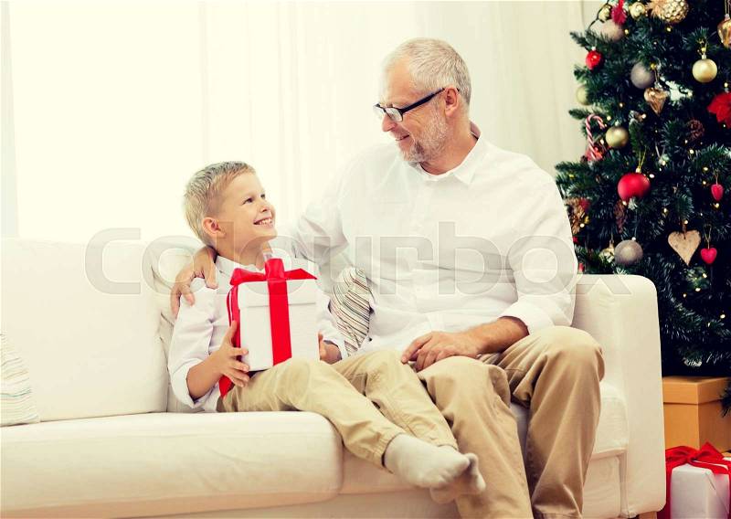 Family, holidays, generation, christmas and people concept - smiling grandfather and grandson with gift box sitting on couch at home, stock photo