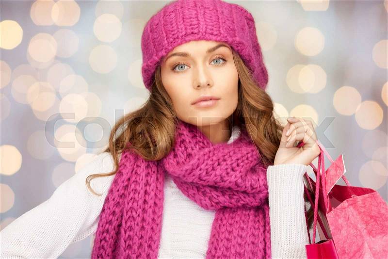 Holidays, christmas, sale and people concept - young woman in winter clothes with shopping bags over lights background, stock photo