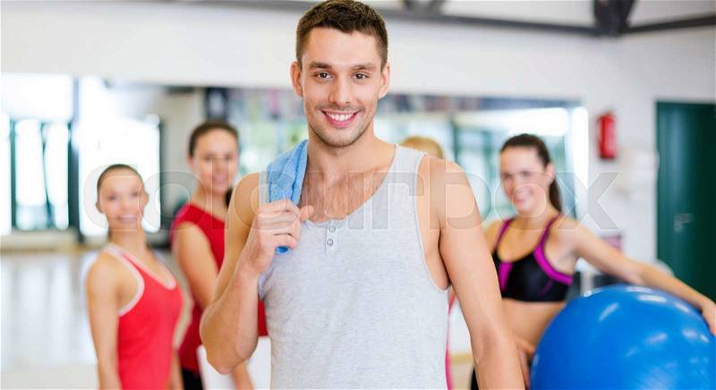 Fitness, sport, training, gym and lifestyle concept - smiling man standing in front of the group of people in gym, stock photo