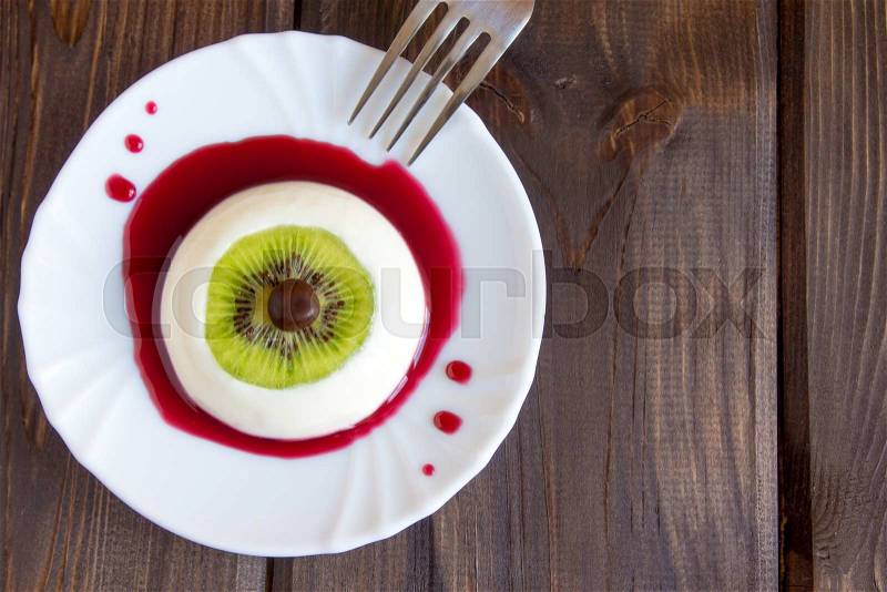Halloween dessert, bloody eye from vanilla panna cotta and kiwi with berry syrup, stock photo
