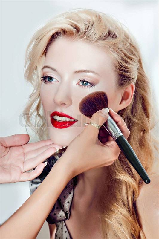 Close up portrait of fashion model.Make up artist applyes cosmetics on her face.Smiling blonde girl.Red lips.Professional.Studio shot.Fashion look, stock photo