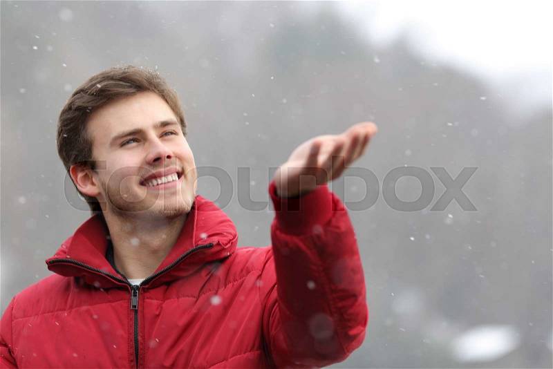 Happy man with a red jacket watching the snow falling on his hand in winter, stock photo