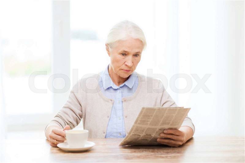 Age, leisure and people concept - senior woman drinking coffee and reading newspaper at home, stock photo