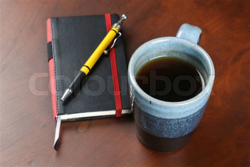 Blue design mug of tea and coffee on wood table with notebook and pen, stock photo