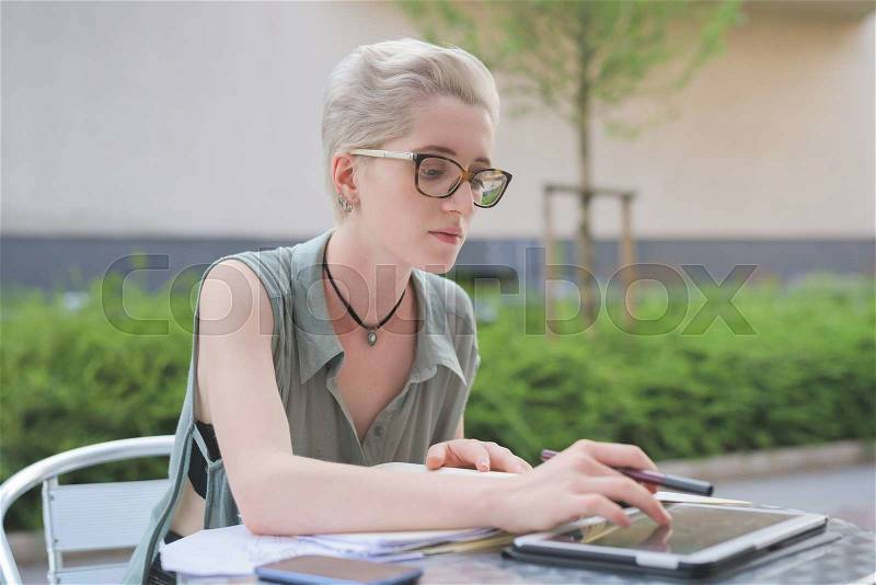 Half length of a young handsome caucasian blonde italian designer sitting in a bar, using a tablet and a smartphone, touching the screen - technology, creativity, working concept, stock photo