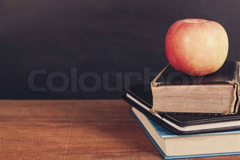 Apple and Books on the wooden desk with Blackboard Background, stock photo