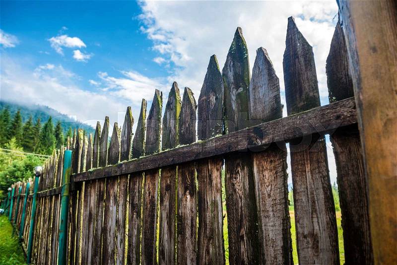 Old country fence with forest and blue sky on background, stock photo
