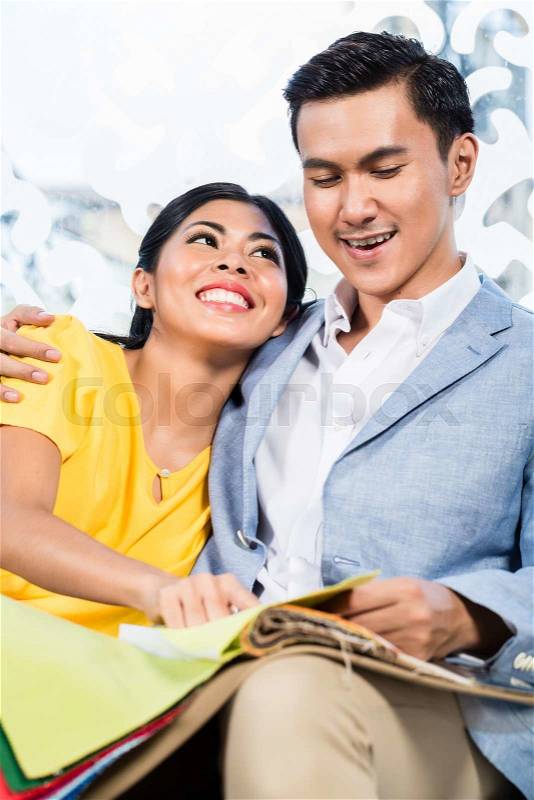 Asian couple buying sofa in furniture store, sitting on couch choosing color and material , stock photo