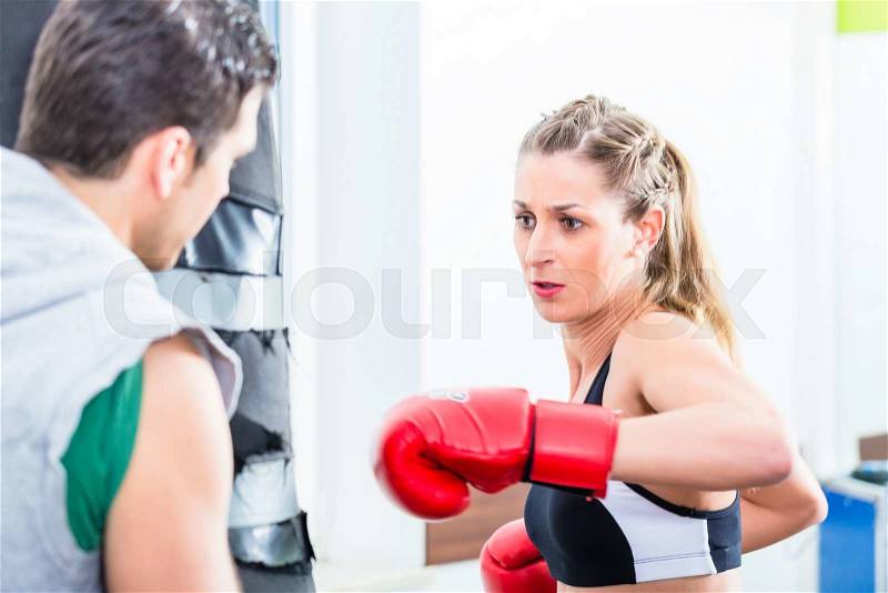 Young woman with trainer in boxing sparring hitting sandbag, stock photo