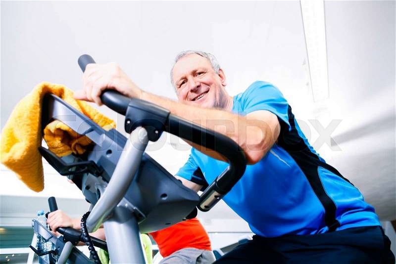 Senior man doing sport on spinning bike in gym looking at camera, stock photo