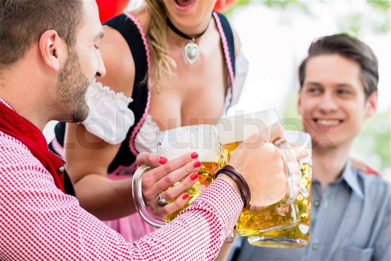 Three friends in Munich Beer garden clinking glasses wearing traditional Tracht, stock photo