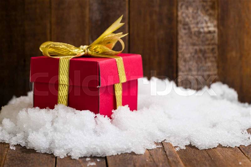 Christmas gift box with a gold ribbon bow on snow, stock photo