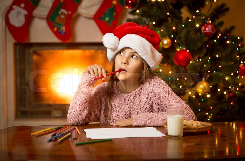 Portrait of thoughtful girl in Santa cap thinking of letter with gift wishes, stock photo