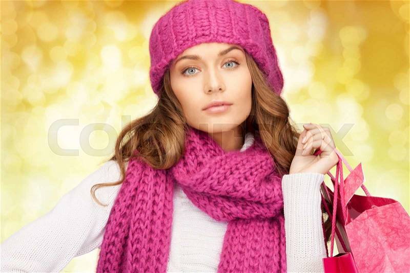 Holidays, christmas, sale and people concept - young woman in winter clothes with shopping bags over lights background, stock photo