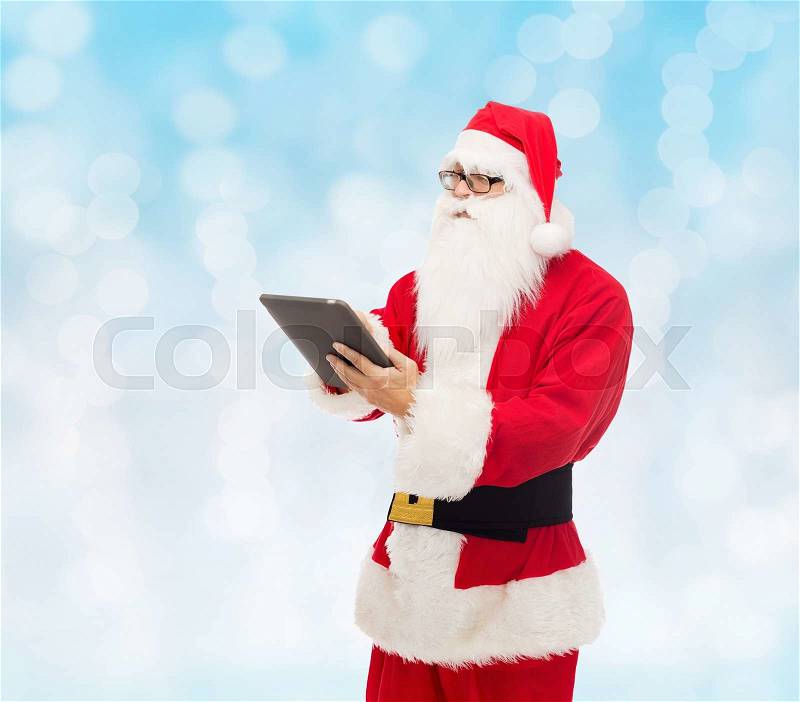 Christmas, holidays, technology and people concept - man in costume of santa claus with tablet pc computer over blue lights background, stock photo