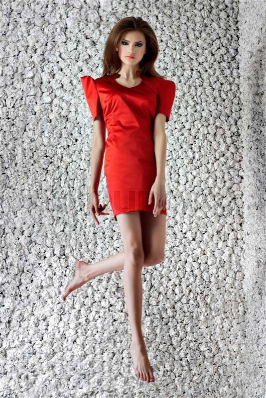 Fashion model poses jumping in design red dress on white paper studio background. Fashion look.Stylish image.Skinny, stock photo
