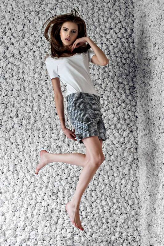Fashion model poses jumping in design white shirt, checkered shorts on white paper studio background. Fashion look.Stylish image.Skinny, stock photo