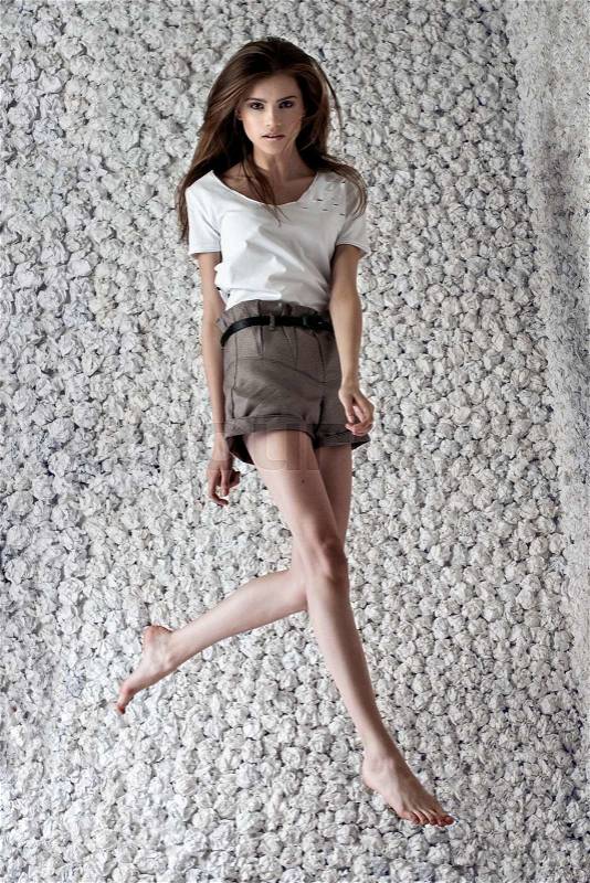 Fashion model poses jumping in design white shirt, checkered shorts on white paper studio background. Fashion look.Stylish image.Skinny, stock photo