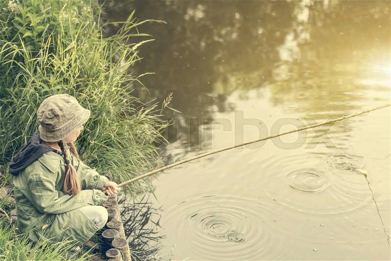 Little fisher girl sitting on a river bank with a rod, stock photo