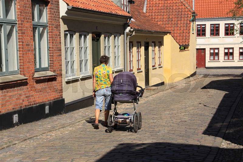 The lady walks with the pram through one of the streets in the residential area in the neighbourhood of H.C. Andersen\'s Hus in Odense in Denmark in the summer, stock photo