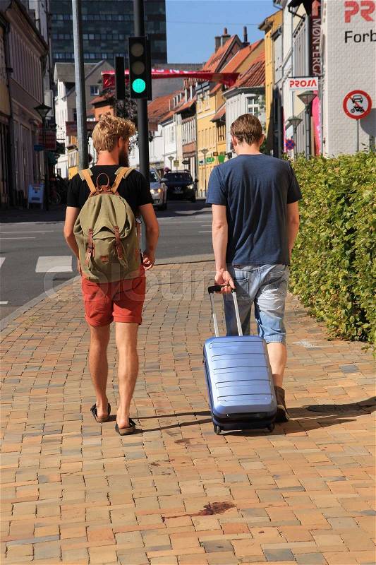Two boyfriends, one with rucksack and the other with a suitcase are walking in the city Odense in Denmark in the summer, stock photo
