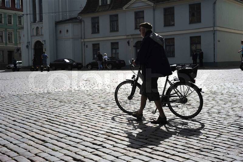 RIGA, LATVIA - AUGUST 9: Man walking his bicycle on an old cobblestone road in Old Town of Riga on August 9, 2010, stock photo