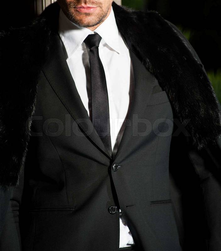 Young handsome businessman wearing stylish suit, tie, white shirt, trousers,black fur coat poses in front of stairs on luxurious interior.Fashion look.Bearded guy.Elegant style, stock photo