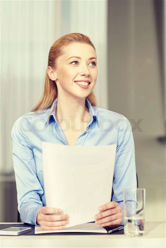Business and people concept - smiling woman holding papers in office, stock photo