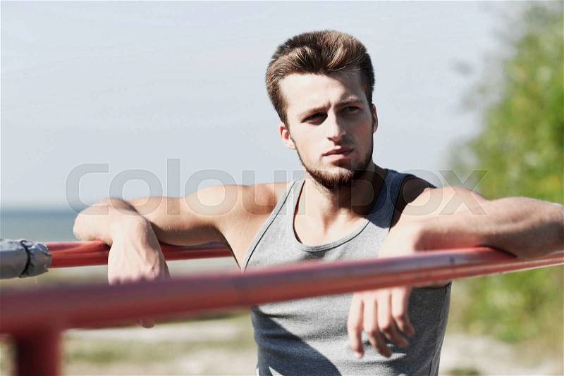 Fitness, sport, training and lifestyle concept - young man exercising on parallel bars outdoors, stock photo