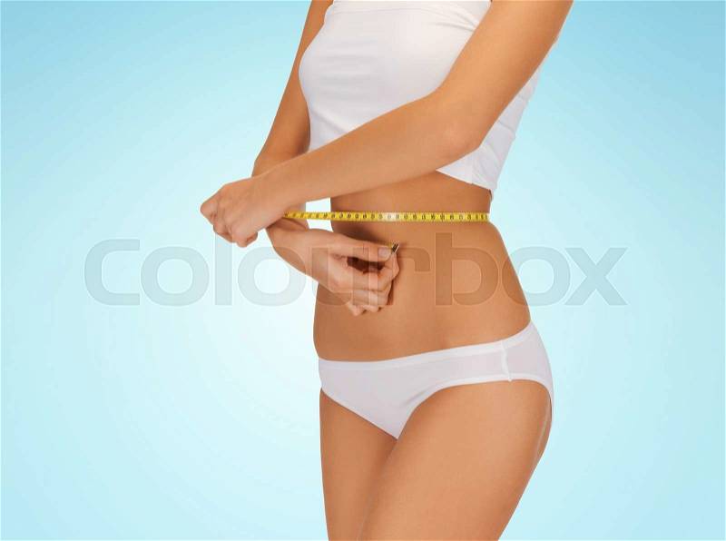 People, beauty, weight loss and diet concept - close up of woman with tape measuring her waist, stock photo