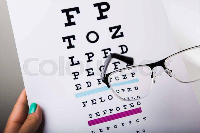 Woman doctor holding eye glasses and exam chart, stock photo
