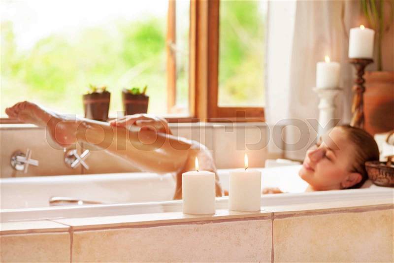 Soft focus photo of gentle young woman lying down in bath tub with foam and candle, enjoying spa procedure in the luxury resort , stock photo