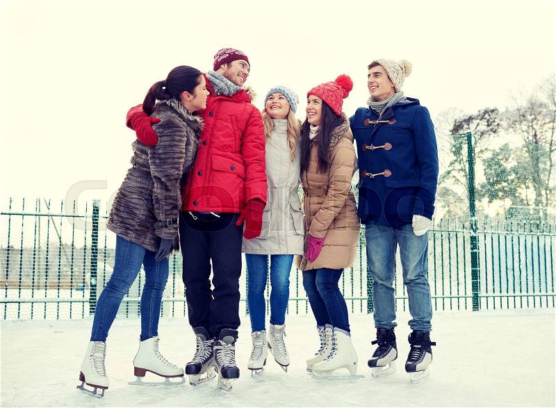 People, winter, friendship, sport and leisure concept - happy friends ice skating and hugging on rink outdoors, stock photo