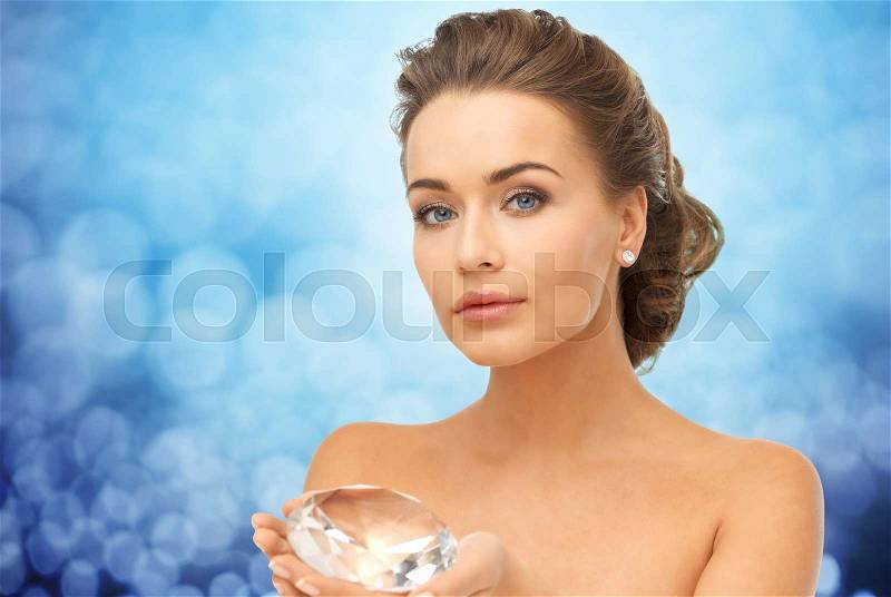 People, jewelry, luxury and beauty concept - woman showing big diamond over blue lights, stock photo
