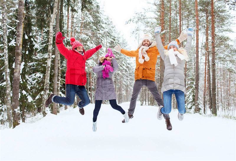 Leisure, season, friendship and people concept - group of smiling men and women having fun and jumping in winter forest, stock photo