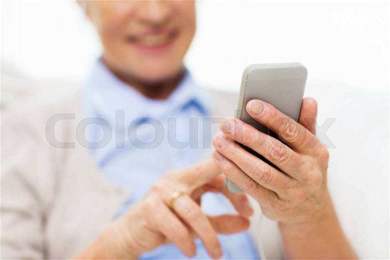 Technology, communication age and people concept - close up of happy senior woman with smartphone texting message at home, stock photo