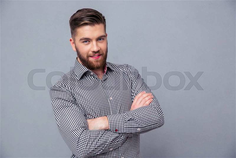 Portrait of a casual man standing in shirt with arms folded over gray background, stock photo