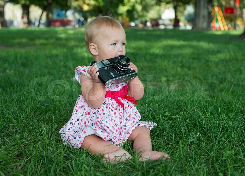 Baby girl is playing with old camera on grass. Baby with camera, stock photo