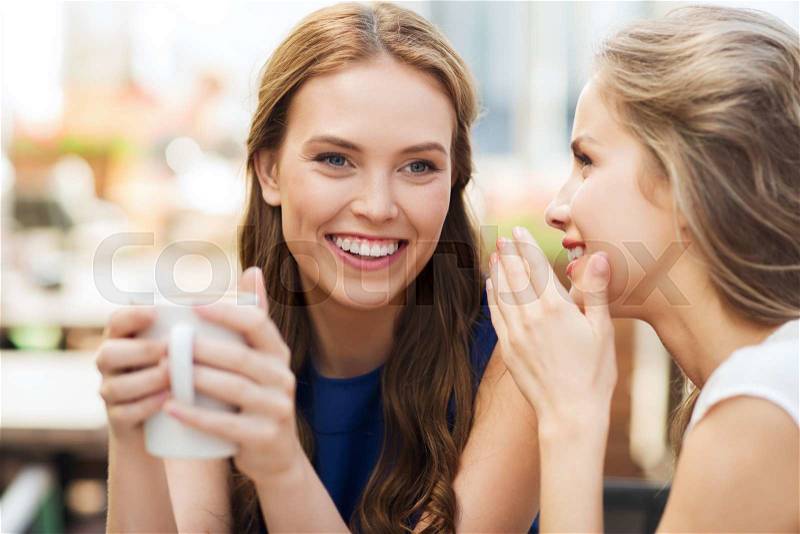 People communication and friendship concept - smiling young women drinking coffee or tea and gossiping at outdoor cafe, stock photo