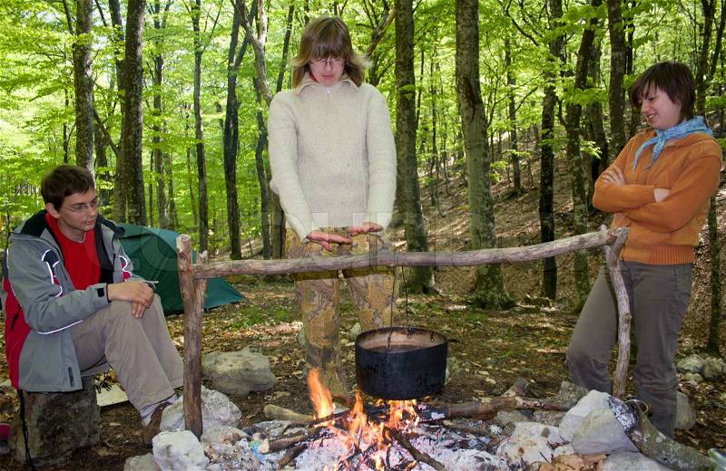 Three tourist sitting near of fire with pot in spring forest, stock photo